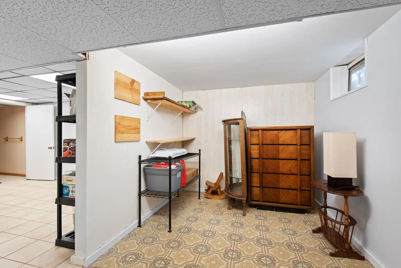 Finished lower-level room with a small high window, wall shelving and wood furniture
