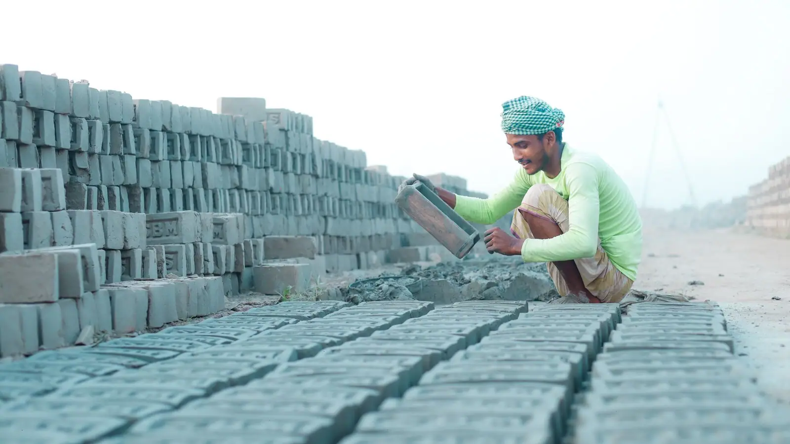 Mason laying concrete blocks beside stacked block pallets on a site