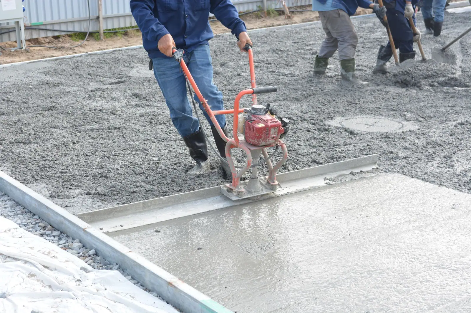 Concrete crew running a power screed across a freshly poured slab