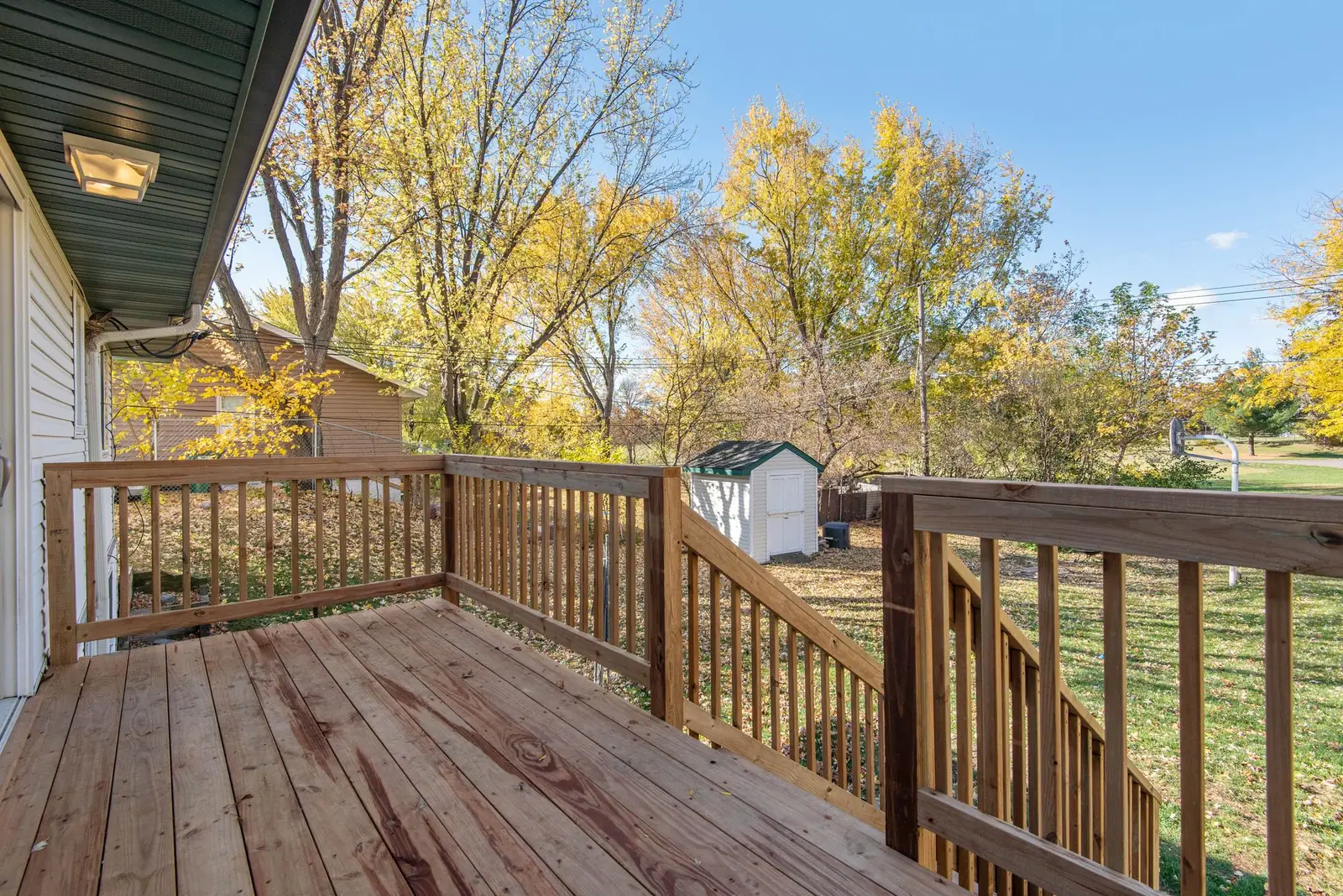 Elevated wood deck with railings overlooking a backyard in fall