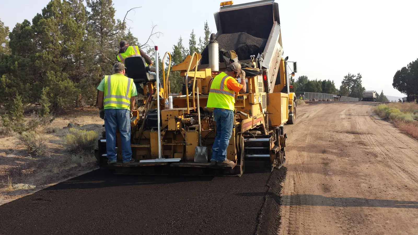 Paving crew in high-visibility vests laying fresh asphalt with a paving machine