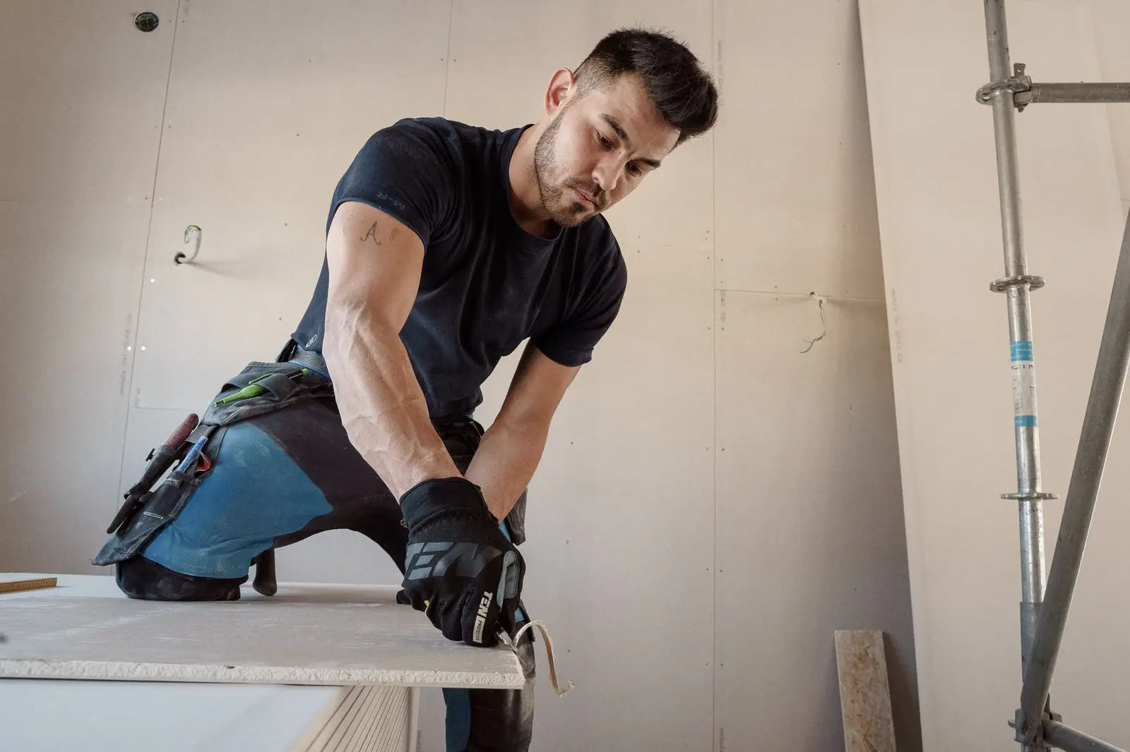 Worker in gloves scoring a sheet of drywall on a work surface