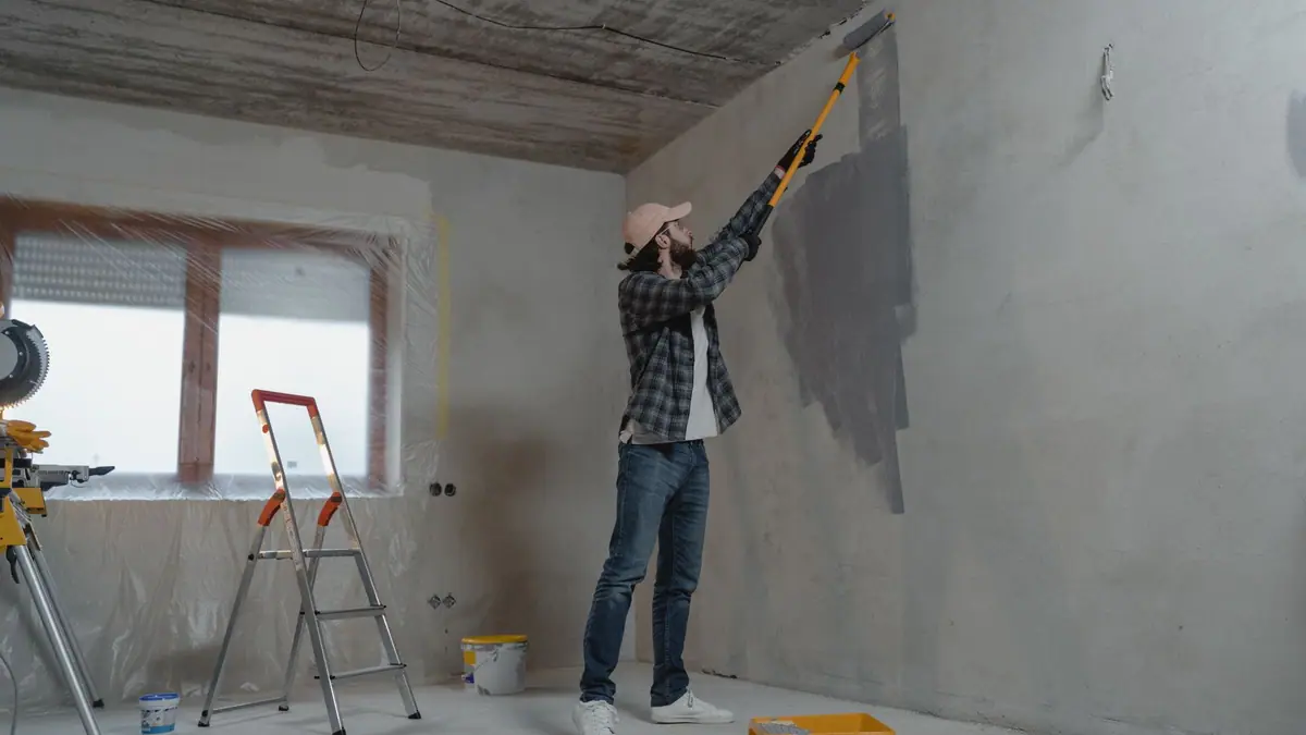 Drywall repair cost: painter finishing a repaired gray interior wall with a roller