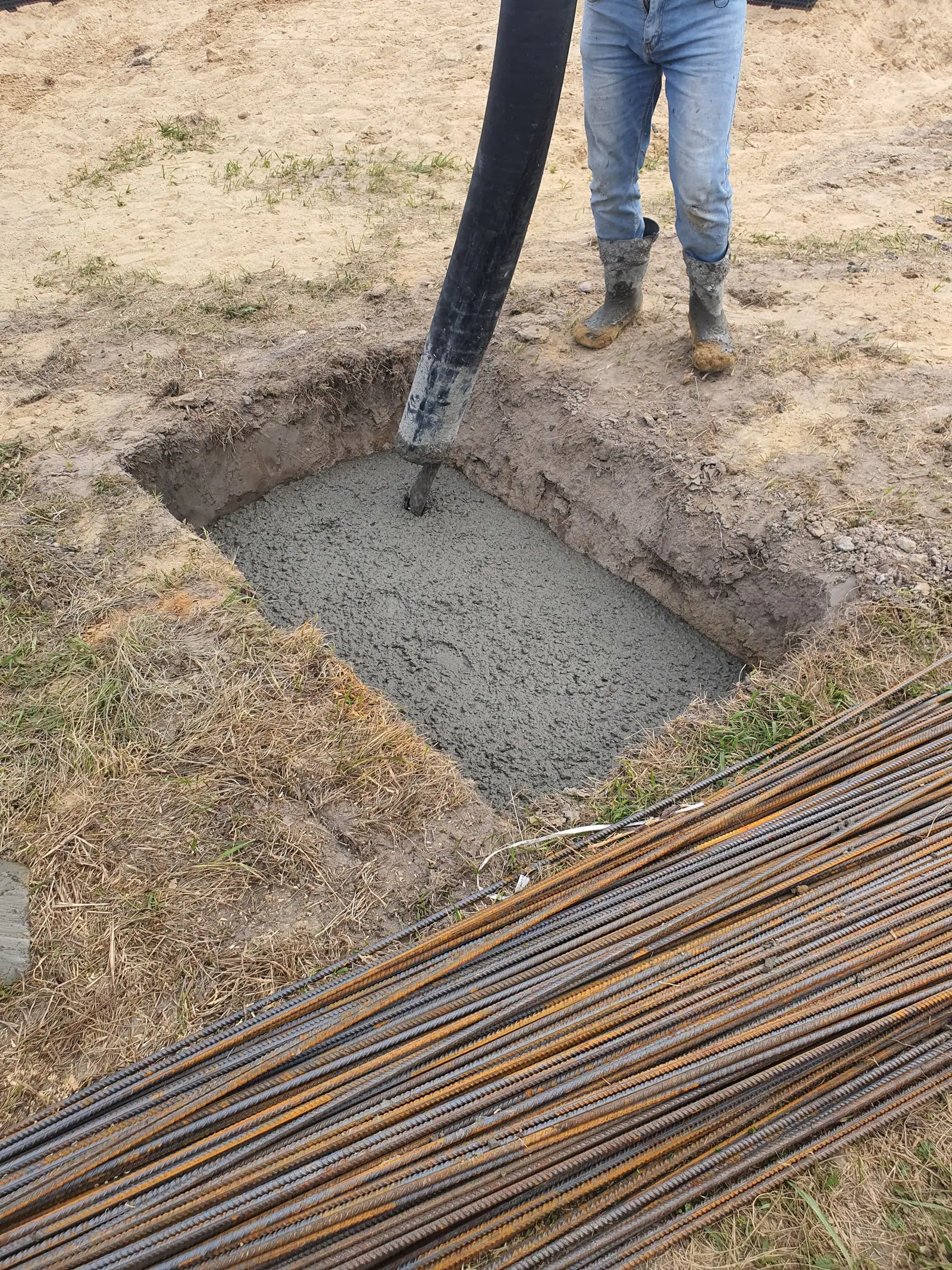 Fresh concrete in a dug footing next to bundled steel rebar at a building site