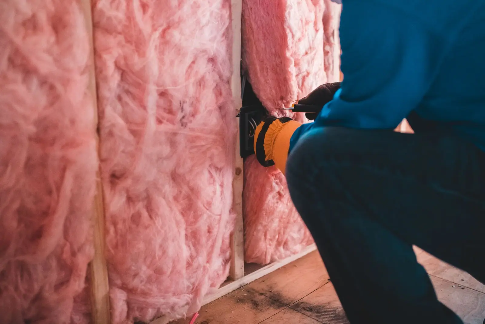 Worker pressing pink fiberglass batt insulation between wall studs