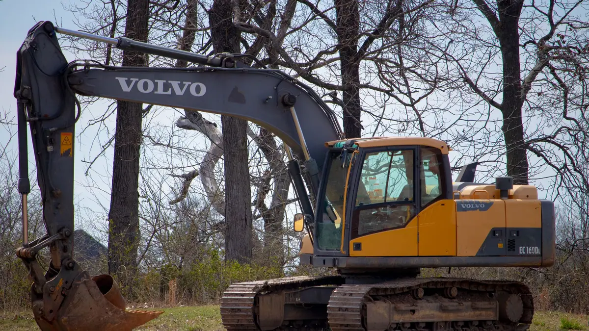 Land clearing cost: excavator on a partly cleared lot beside mature trees