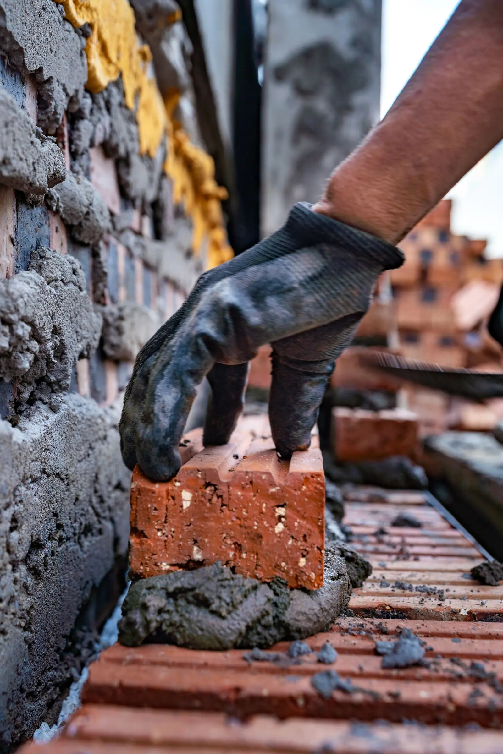 Gloved bricklayer setting a red brick into a fresh mortar bed