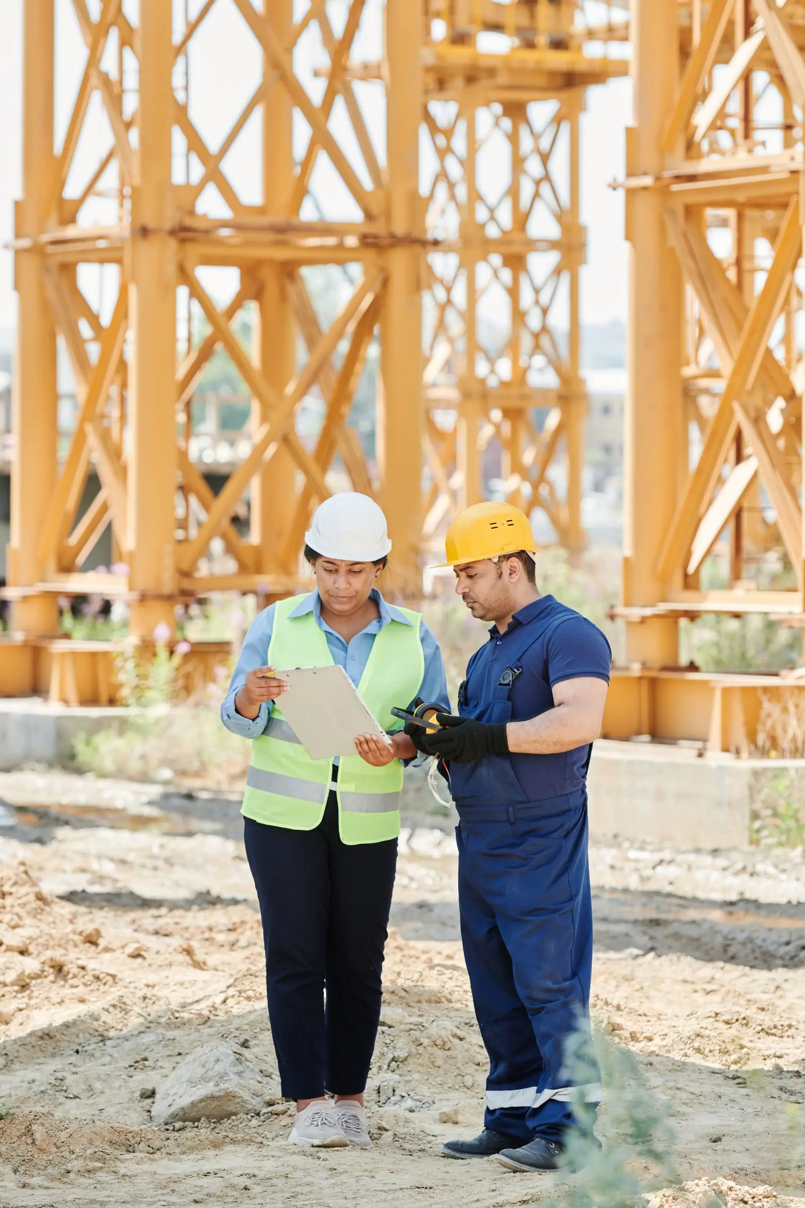 Two builders in hard hats and safety vests reviewing plans on a construction site