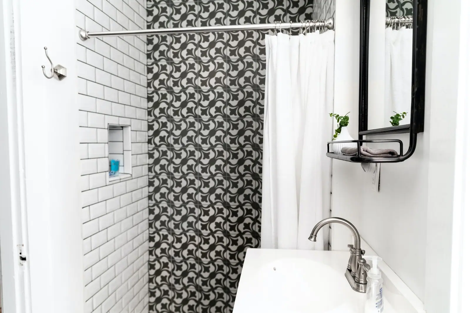 White subway tile shower wall beside a black-and-white patterned tile accent wall