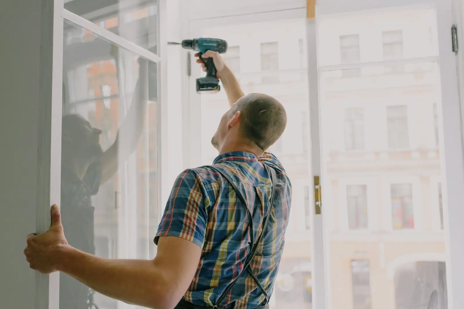Installer drilling a new white window frame into the rough opening of a house